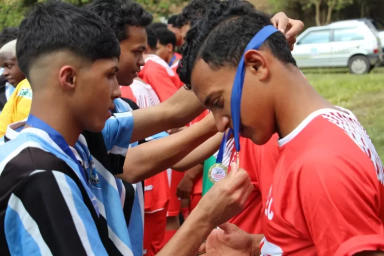 Jogador, com camisa azul, preta e branca, entrega medalha ao adversário, que usa camisa vermelha com detalhe em branco, no encerramento das finais do futebol de base de Mariana