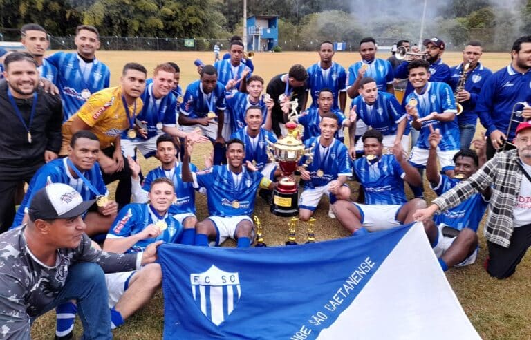 Atletas e dirigentes do São Caetanense, campeão dos juniores em mariana, comemoram o título, tendo ao centro a taça conquistada