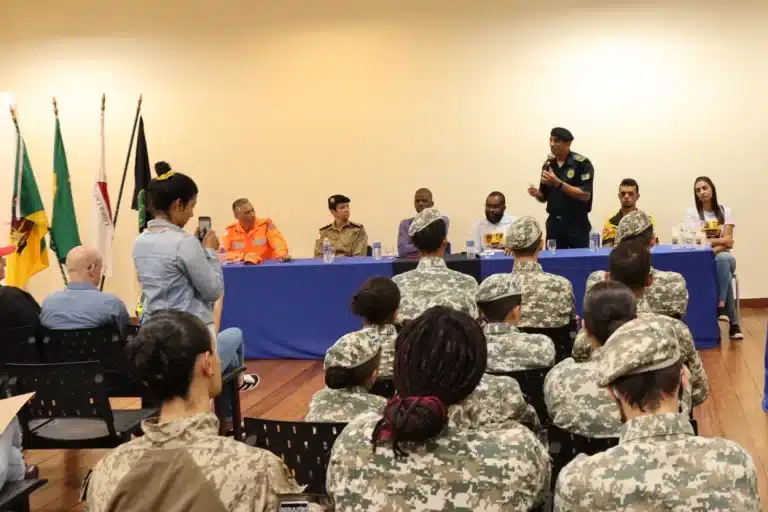 Em primeiro plano, plateia acompanha a abertura na Semana Nacional de Trânsito em Mariana. Ao fundo, os integrantes da mesa, com um deles, ao microfone, fazendo seu depoimento.