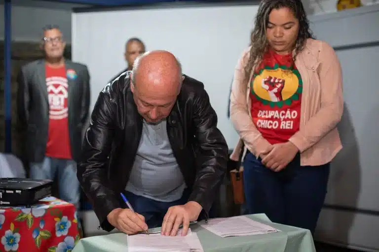 Prefeito de Ouro Preto, Angelo Oswaldo, assina decreto municipal sobre processo de regularização fundiária do bairro Taquaral. Ao lado, Stefane Malaquias, vestida com a camisa da Ocupação Chico Rei. Ao fundo, o vereador Wanderley Kuruzu, com camisa do MTST, e ao seu lado o secretário de Desenvolvimento Social Edvaldo César Rocha