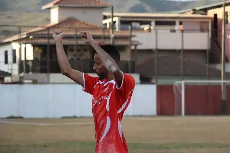 Jogador do Olimpic, de uniforme vermelho com detalhes em branco, comemora com dancinha gol marcado contra o Guarany, em partida válida pelo Campeonato de Mariana