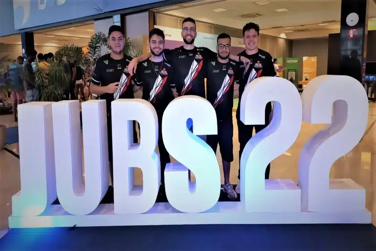 Integrantes da equipe de eSport da UFOP, em registro feito na sede dos Jogos Universitários Brasileiros, com símbolo da edição 2022 à frente