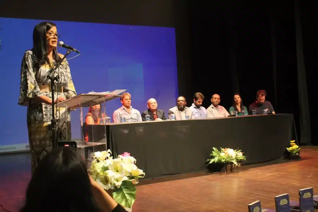 Cibele Aparecida utiliza a tribuna do Cine Theatro Municipal, tendo ao fundo a mesa com as autpridades presentes ao evento