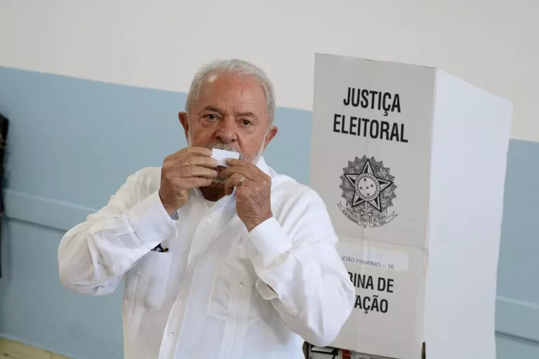 De camisa branca, à frente de uma cabine de votação, o candidato Lula beija o comprovante de sua votação