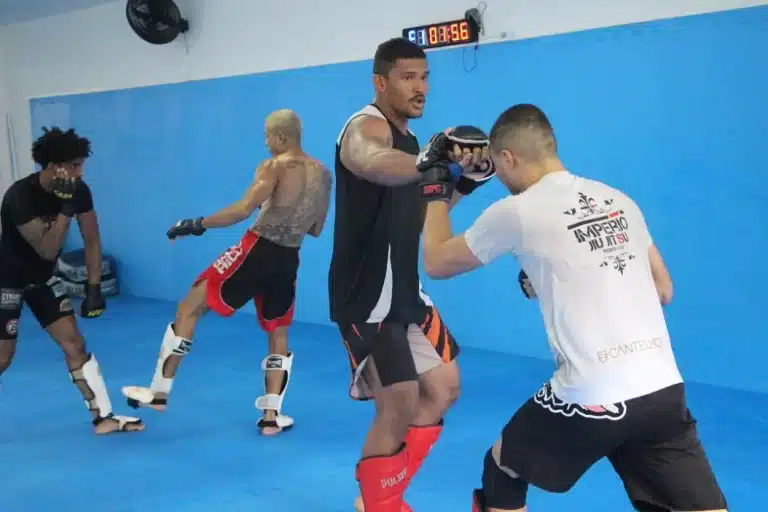 Em local com piso e paredes revestidas com borracha azul, 4 lutadores de MMA fazem treinamento de kickboxing