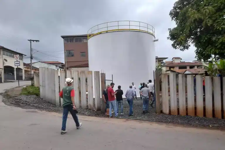 Pessoas presenciam evento, vendo´se um reservatório cilíndrico e cervamento de concreto.