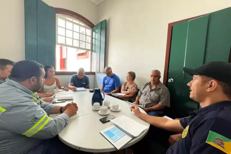 Pessoas em volta de mesa branca, cm garrafa de café e xícaras em cima, debatem os problemas da Rua João Batista