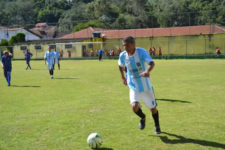 Jogador do Trovão Azul, com calção branco e camisa azul e branca, conduz a bola em jogo contra o Tabajaras